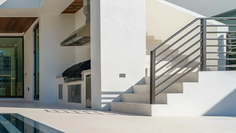 Built in poolside outdoor kitchen with a vent hood and stainless doors at a white Florida home