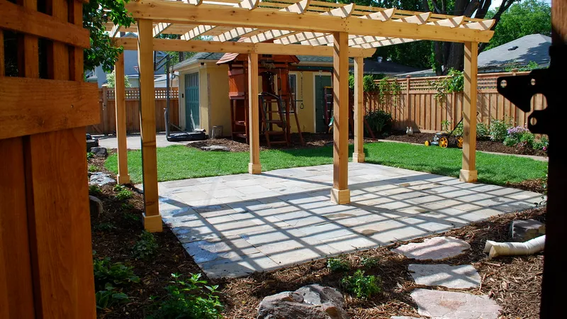Wood pergola over a stone paver patio in a backyard